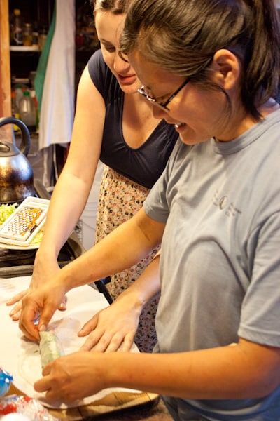 Two women assembling vegetable summer rolls in a kitchen.