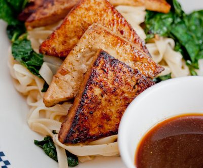 Tofu over kale and noodles with dipping sauce.