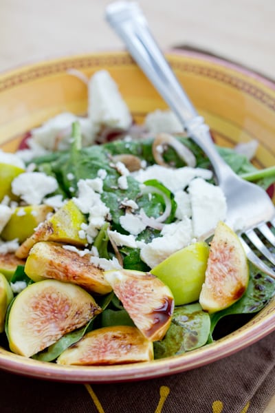 A bowl of salad topped with figs and goat cheese.