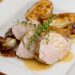 A plate of sliced pork tenderloin with pears and shallots, garnished with fresh thyme.
