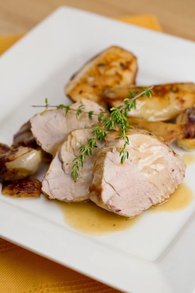 A plate of sliced pork tenderloin with pears and shallots, garnished with fresh thyme.
