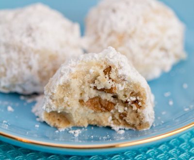 Mexican wedding cookies on a plate with a bite taken out of one.