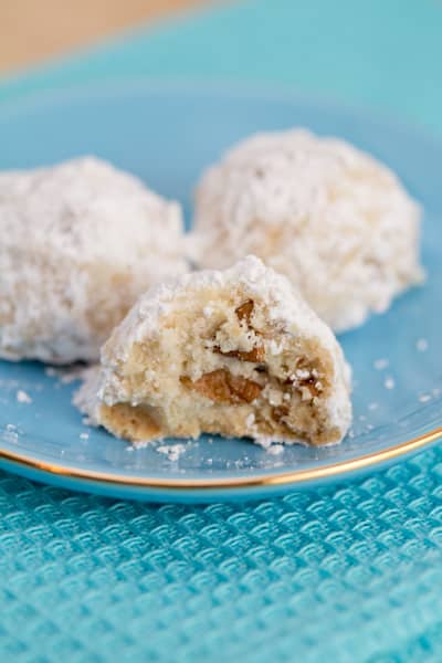 Mexican wedding cookies on a plate with a bite taken out of one.