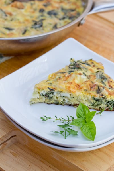 Siced omelet on a plate with fresh herbs.