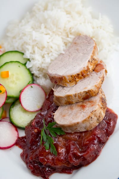 Sliced pork tenderloin with sauce, veggies, and rice.