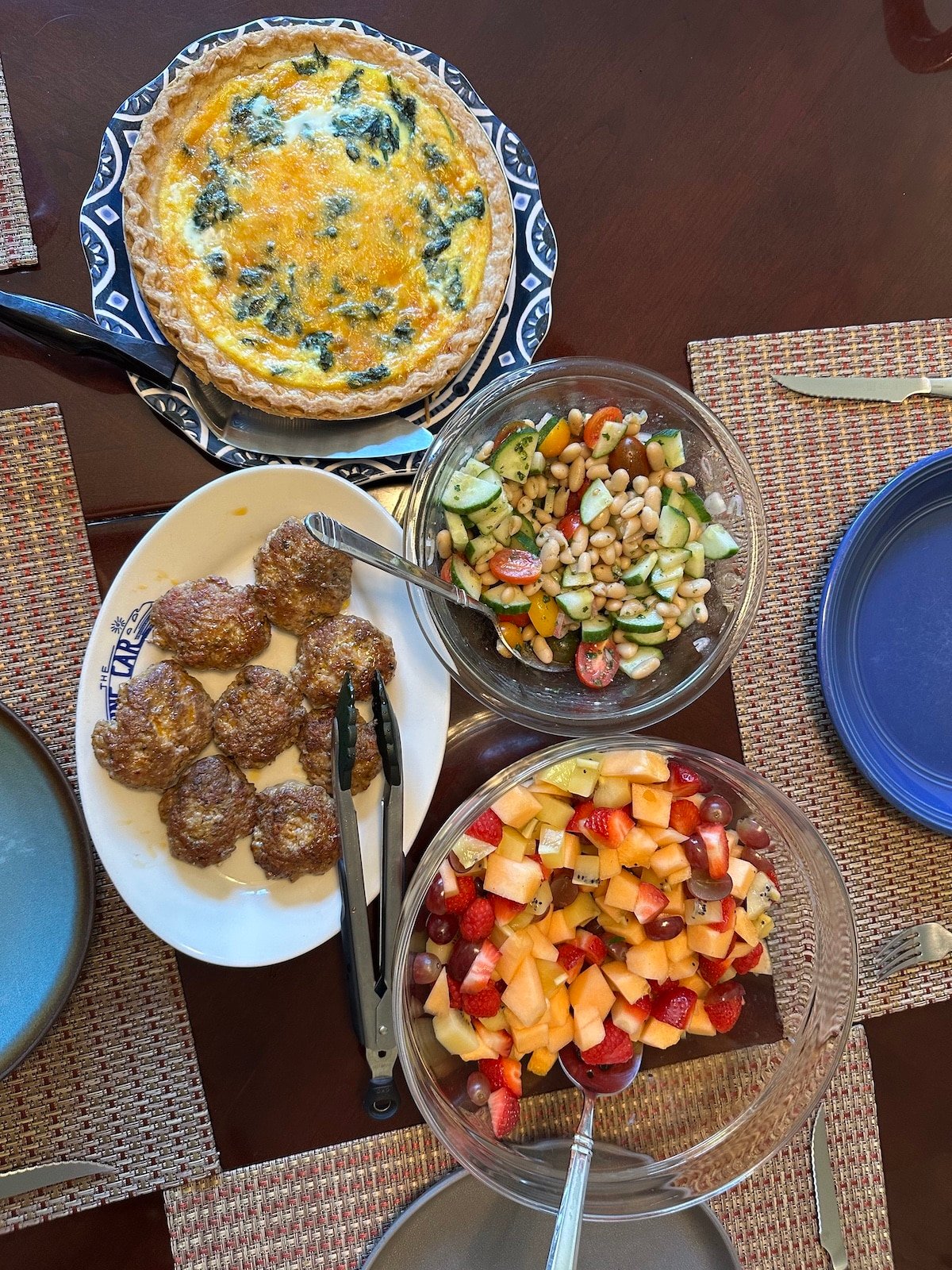 Brunch spread with quiche, fruit salad, breakfast sausage patties, and bean salad
