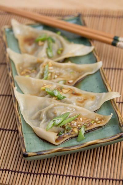 A platter of dumplings topped with sauce and green onions.