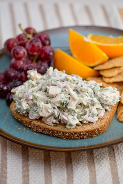 A plate of chicken salad with dill on a slice or bread with fresh fruit alongside.