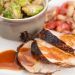 A plate of sliced pork tenderloin with brussels sprouts and a tomato bean salad.