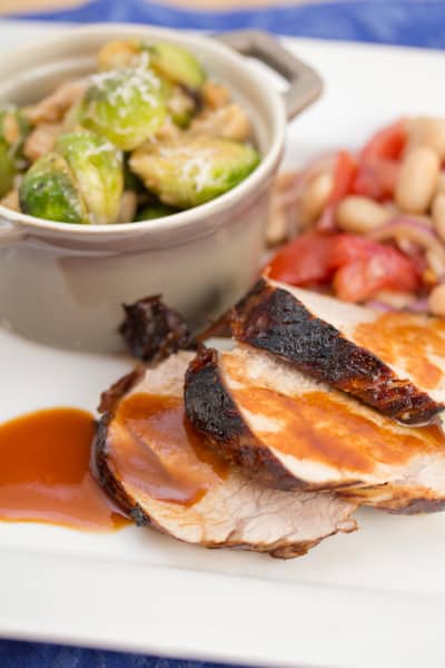 A plate of sliced pork tenderloin with brussels sprouts and a tomato bean salad.