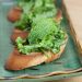A close-up of crostini topped with fava bean, arugula, and mint.