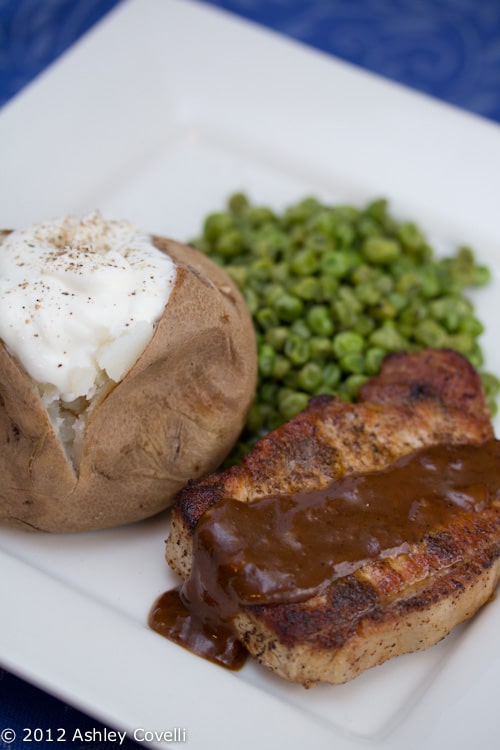 Pork chop and gravy with peas and a baked potato.
