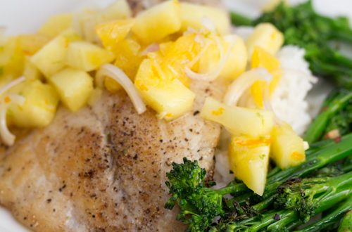 A plate of tilapia with pineapple salsa and broccolini.