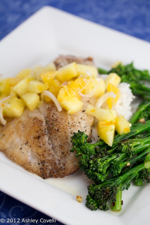 A plate of tilapia with pineapple salsa and broccolini.