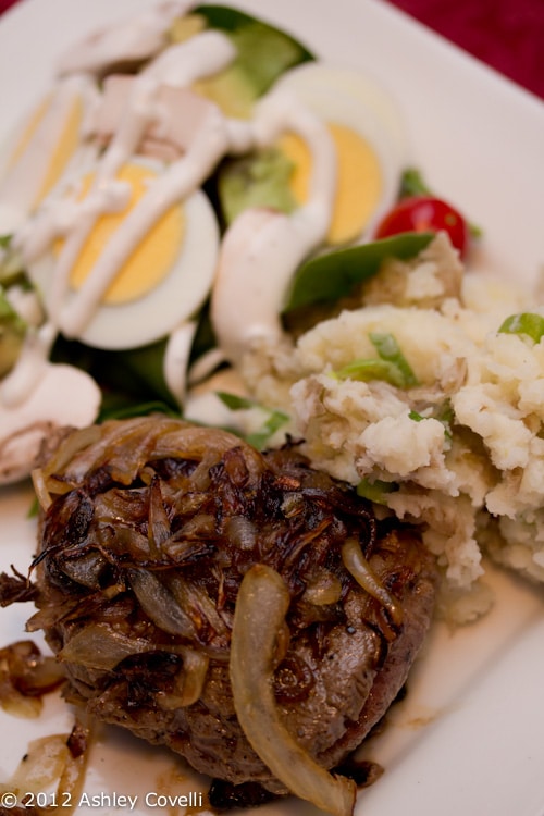 A plate of steak with caramelized onions, salad, and mashed potatoes.