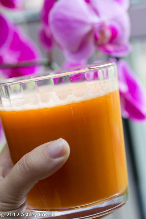 Hand holding a class of fresh juice with orchids in the background.