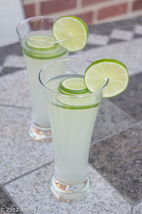 Two glasses of honey limeade garnished with lime wheels.