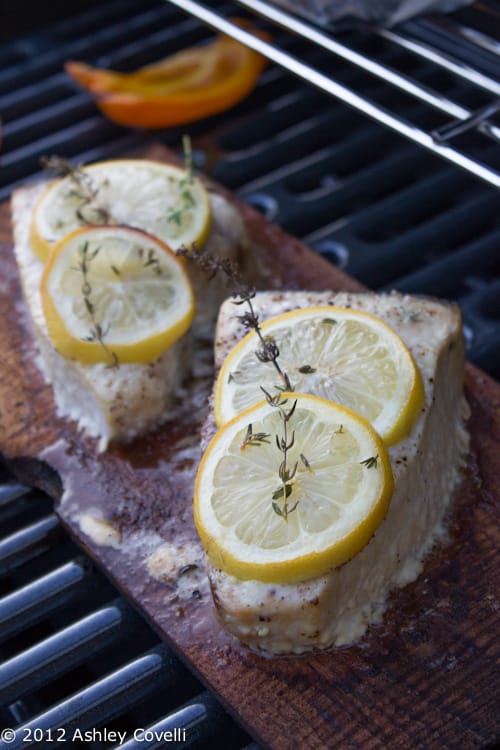 Swordfish topped with lemon and thyme being grilled on a cedar plank.