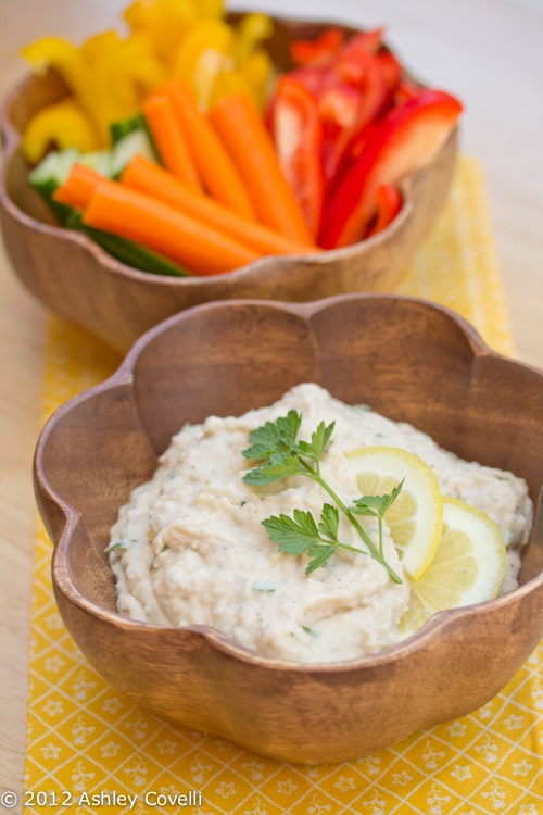 A bowl of lemon-garlic white bean dip with raw veggies alongside.