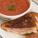 A bowl of gazpacho with a grilled ham and cheese sandwich.