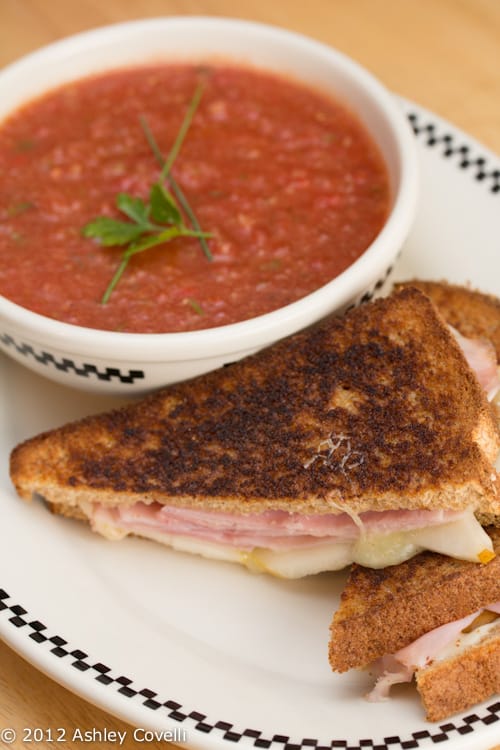 A bowl of gazpacho with a grilled ham and cheese sandwich.