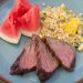 Steak on a plate with quinoa corn salad and fresh watermelon.
