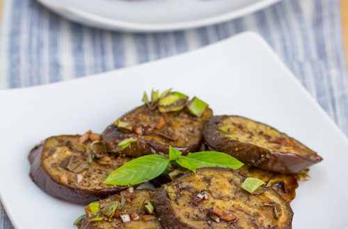 Marinated eggplant salad on 2 plates with fresh basil garnish.