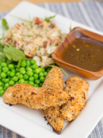 Chicken tenders on a plate with peas, dipping sauce, and quinoa salad.