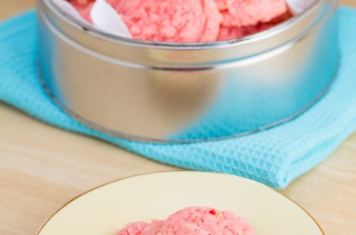 A tin of pink cookies with a plate alongside.