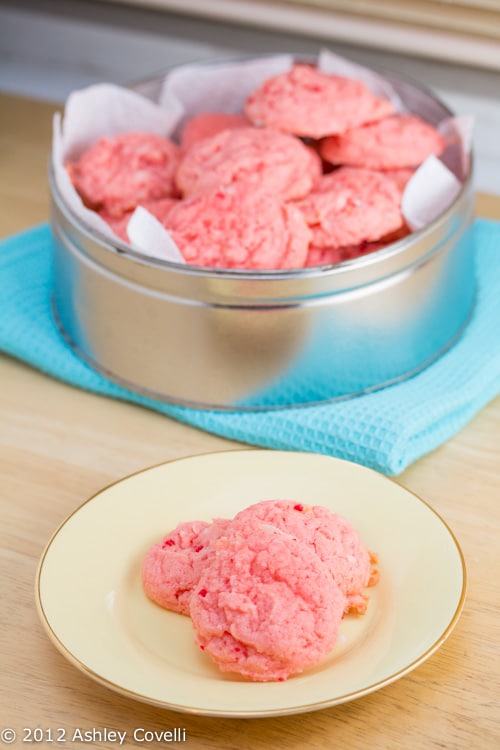 A tin of pink cookies with a plate alongside.