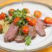 A plate of flank steak topped with tomatoes over orzo.