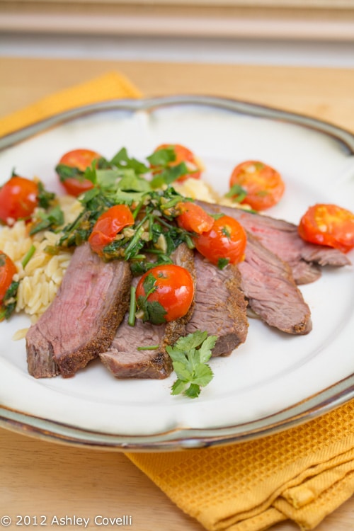 A plate of flank steak topped with tomatoes over orzo.