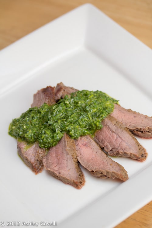 A plate of flank steak topped with chimichurri.