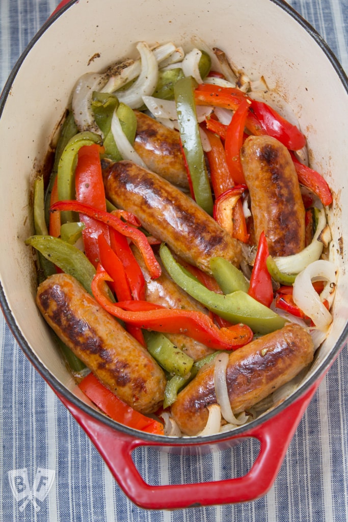 Overhead view of a dutch oven filled with sausages, peppers, and onions.