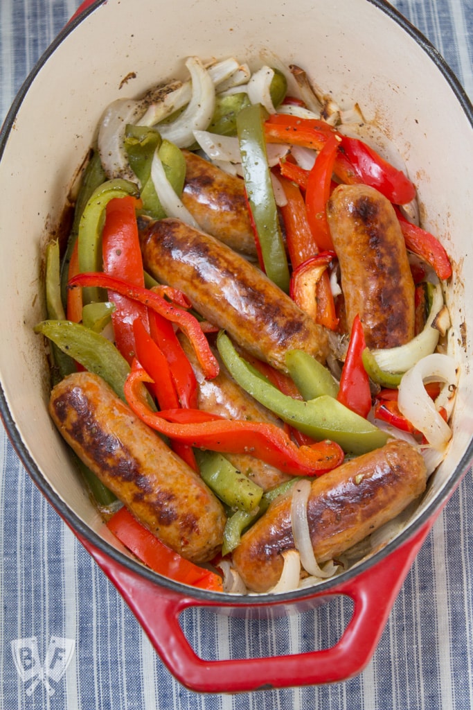 Overhead view of a Dutch oven full of sausage, peppers, and onions.