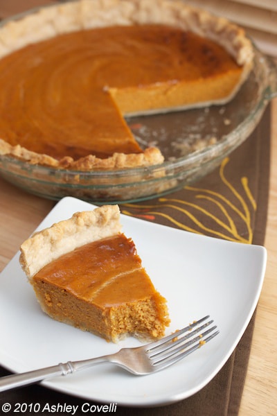 Pumpkin pie with a slice on a plate and a bite taken out of it.