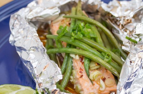 Plate with a foil packet of glazed salmon and green beans with a lime wedge for garnish.