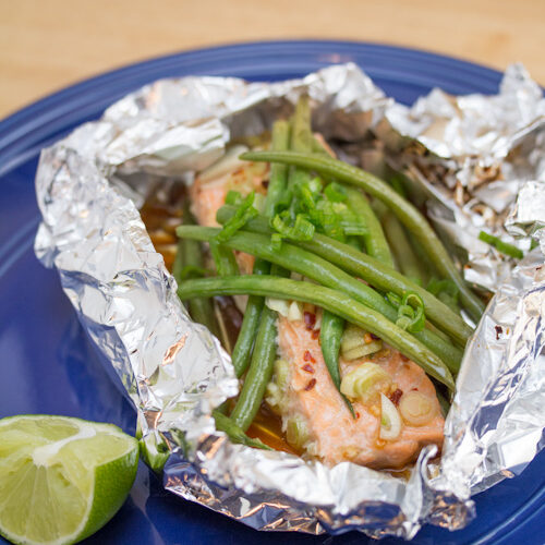 Plate with a foil packet of glazed salmon and green beans with a lime wedge for garnish.