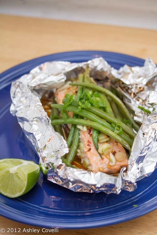 Plate with a foil packet of glazed salmon and green beans with a lime wedge for garnish.