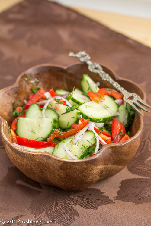 Bowl of cucumber salad with red bell peppers and dill.