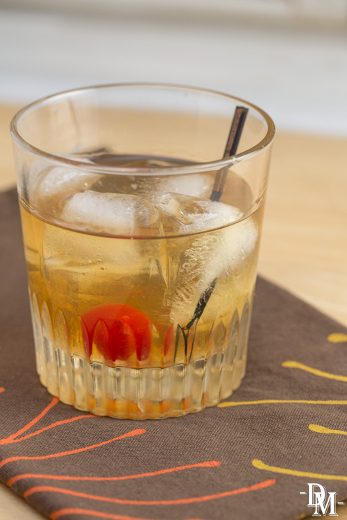 Old fashioned cocktail in a glass with a maraschino cherry.