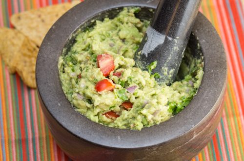 Mortar and pestle with toasted spice guacamole surrounded by tortilla chips.