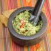 Mortar and pestle with toasted spice guacamole surrounded by tortilla chips.