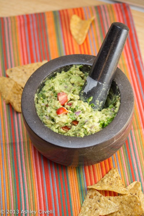 Mortar and pestle with toasted spice guacamole surrounded by tortilla chips.