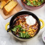 Overhead view of bowls of Spicy Turkey Three-Bean Chili with toppings and cornbread alongside.