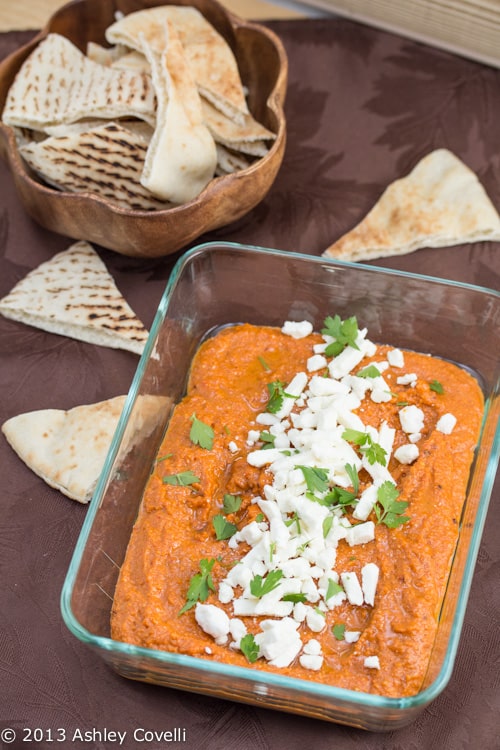 Muhammara in a serving dish topped with feta cheese alongside pita bread.