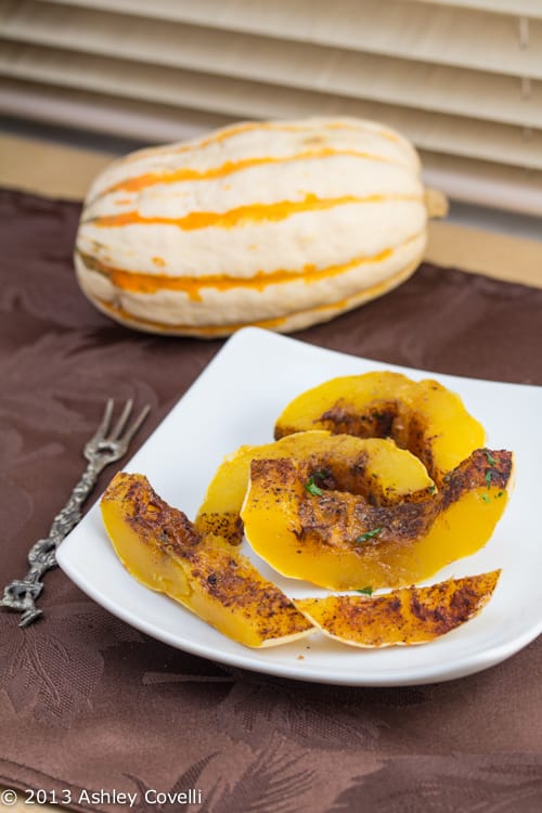 Roasted delicata squash on a plate with a whole squash in the background.