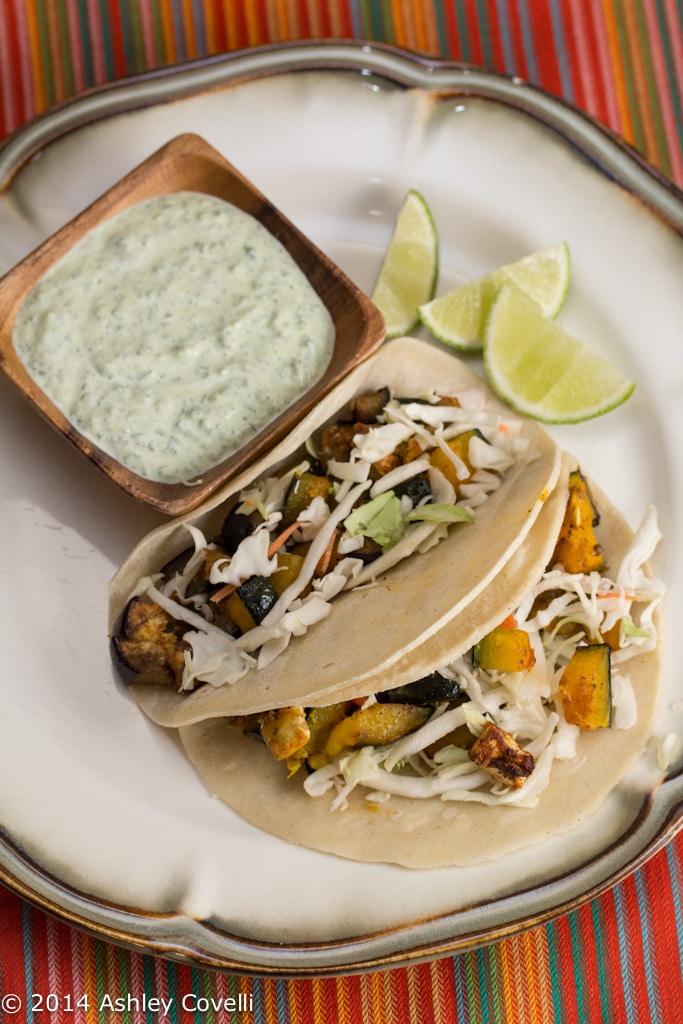 A plate of Roasted Kabocha and Eggplant Tacos with Poblano Crema and lime wedges.