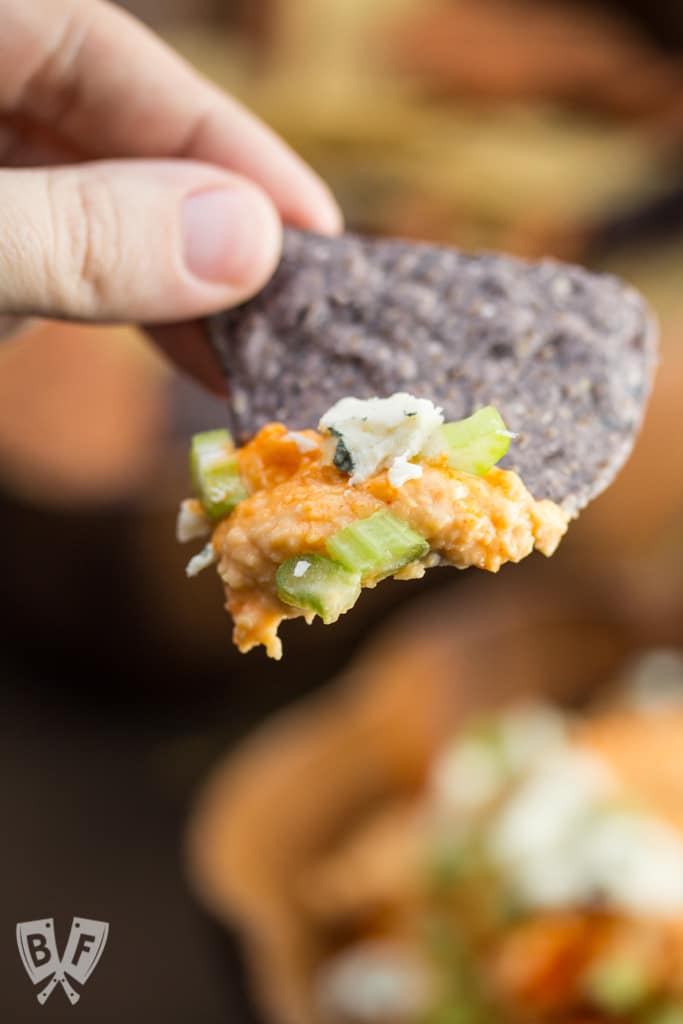 Dipping a blue tortilla chip into Buffalo chickpea dip