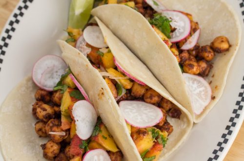 Overhead view of a plate with 3 Spiced Chickpea Tacos with Cilantro-Peach Relish and lime wedges.